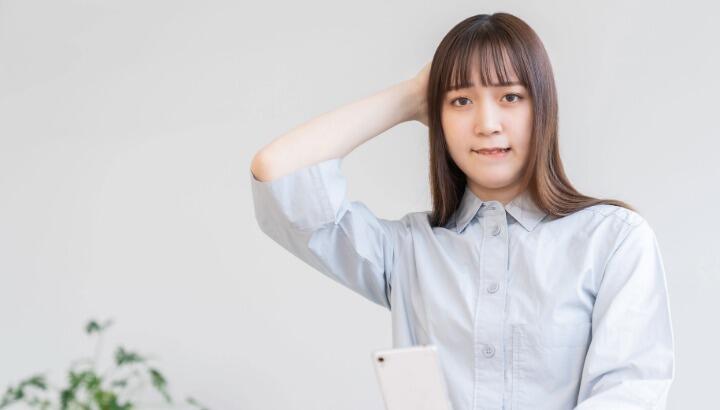 スマホをもって頭に手を当てる女性